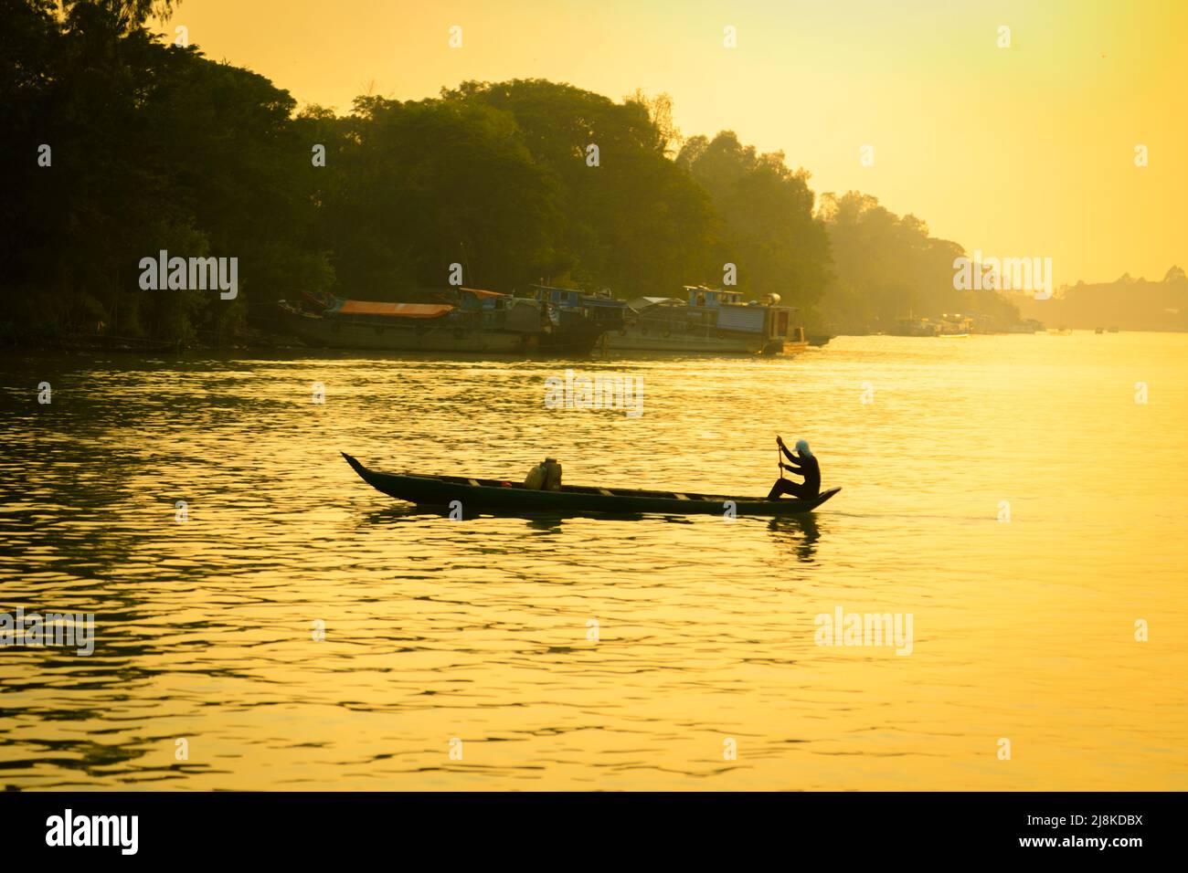 On the Mekong River between Cambodia and Vietnam with a small wood boat and one person in silhouette. Stock Photo