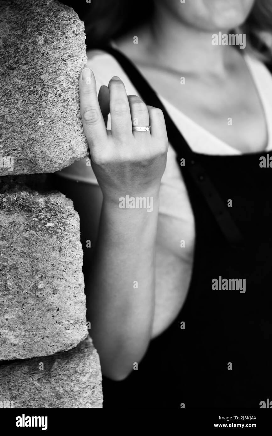 A black and white photograph of a woman standing against a wall. The hand with the ring is in focus. Vertical photo. Stock Photo