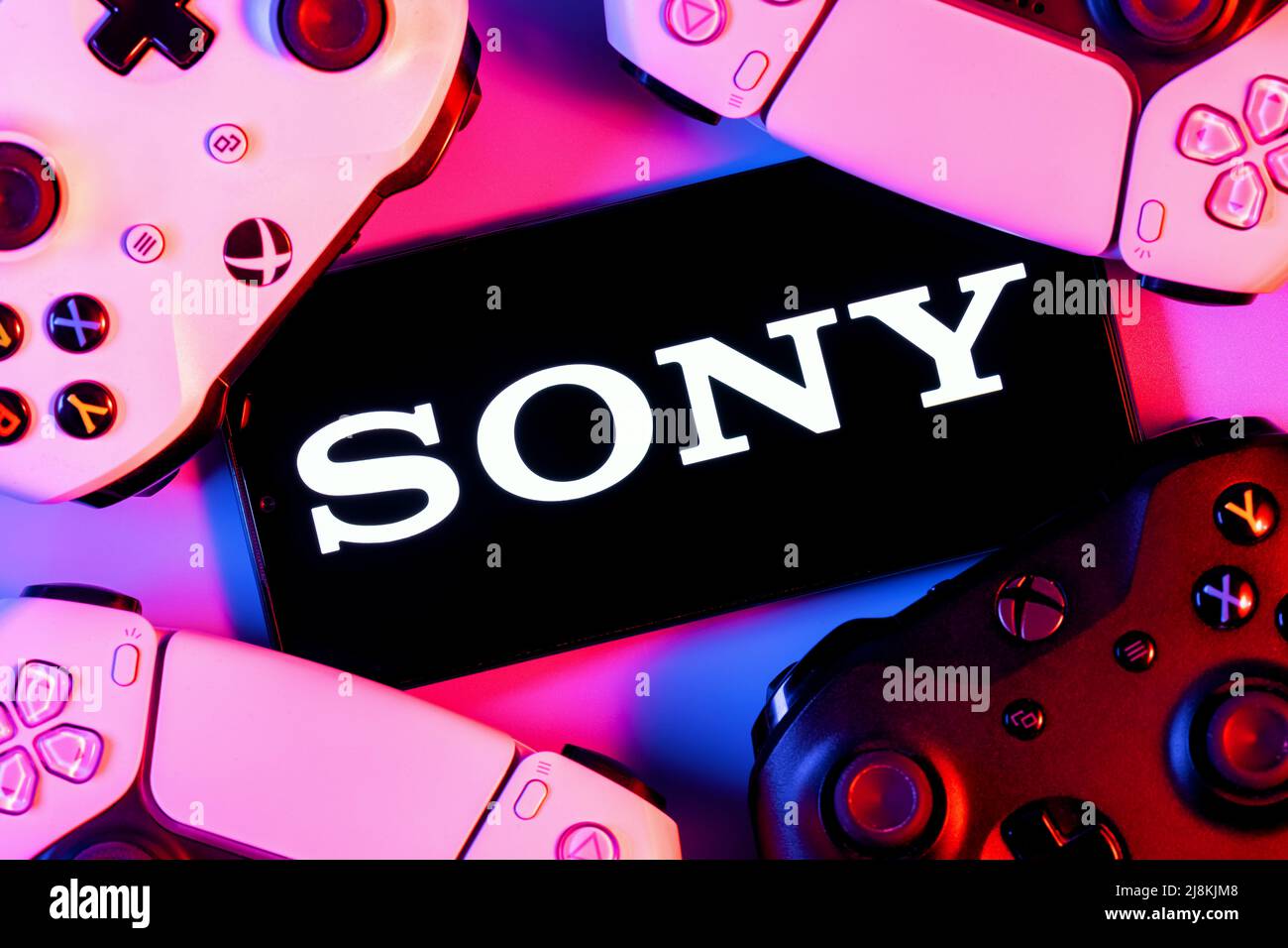Smartphone with SONY logo on screen surrounded by gamepads. Stock Photo