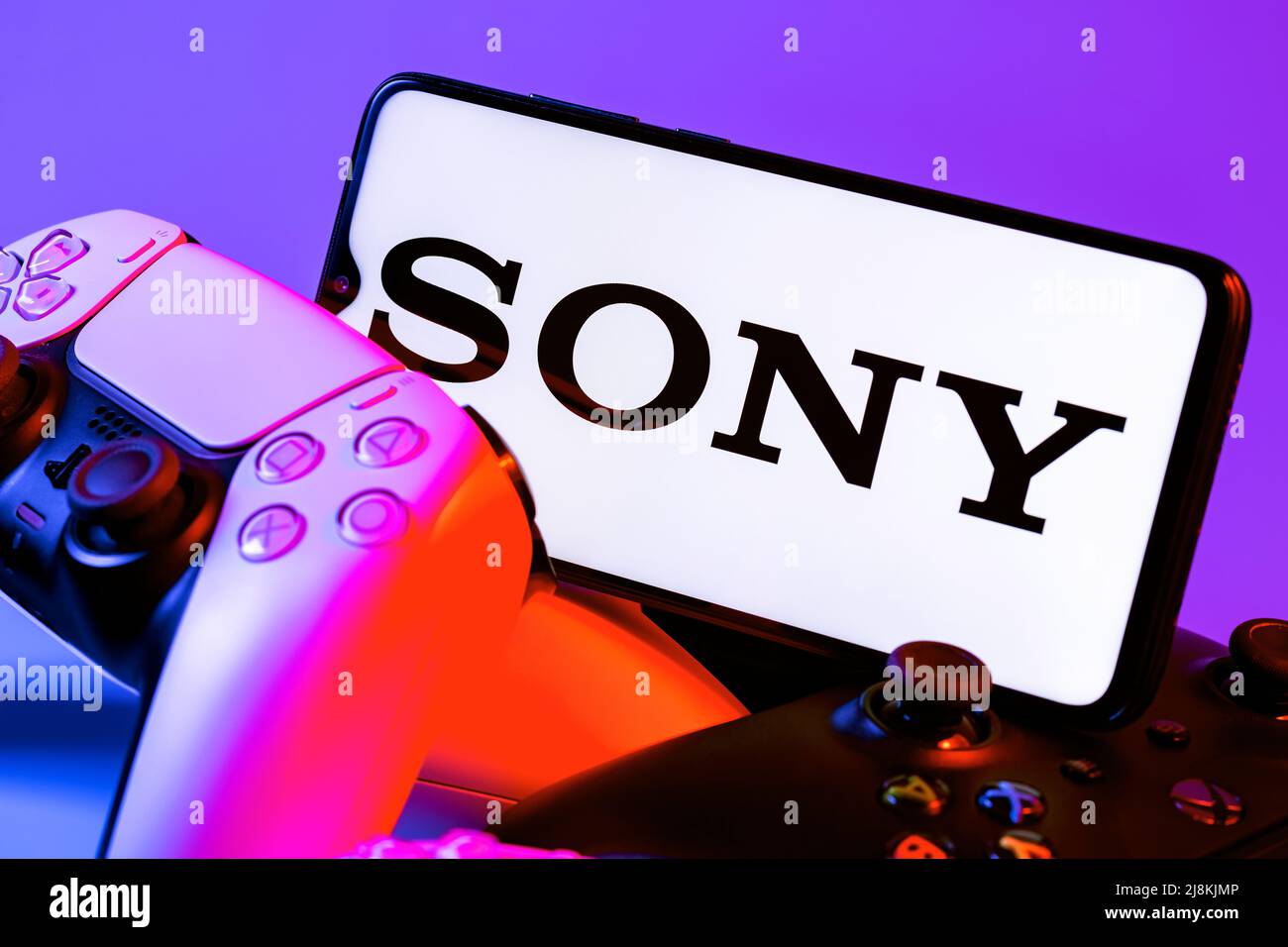 Smartphone with SONY logo on screen on pile of gamepads. Stock Photo