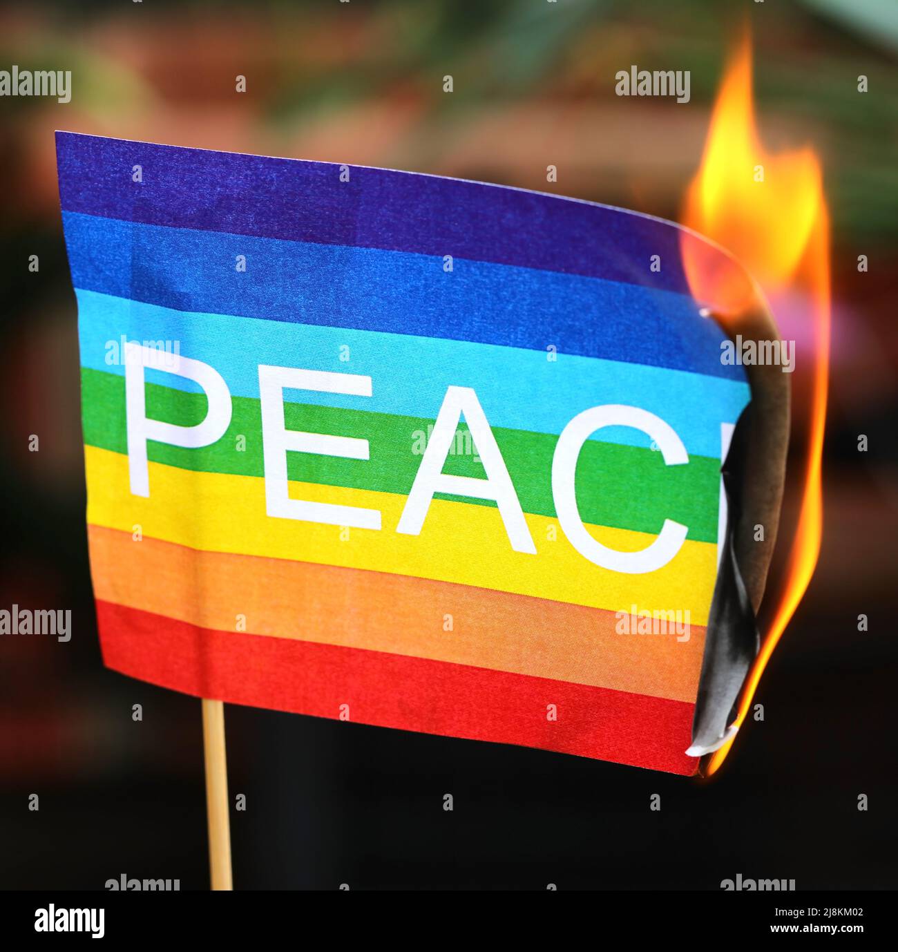 Peace flag with the text and the colors of the rainbow as it catches fire symbolizing the never-ending war Stock Photo