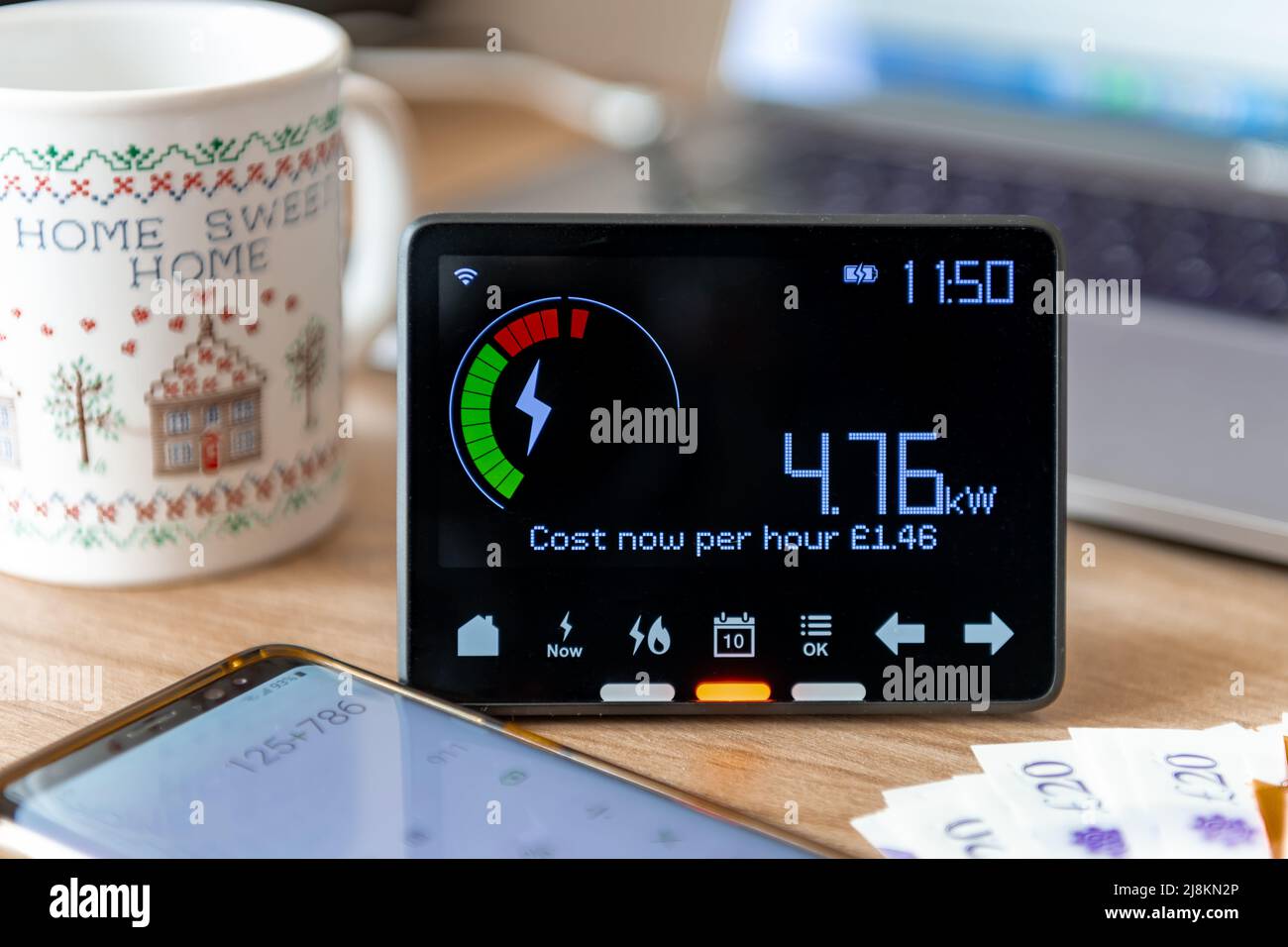 A rising home energy cost concept with a smart meter, bank notes, calculator and tea mug. Stock Photo