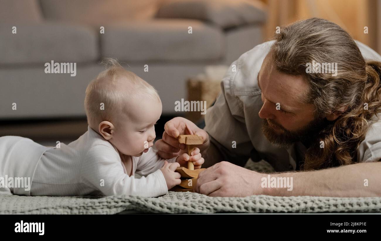 Caucasian family bearded father daddy dad with little daughter son baby infant newborn toddler playing at home on floor with toys collecting wooden Stock Photo
