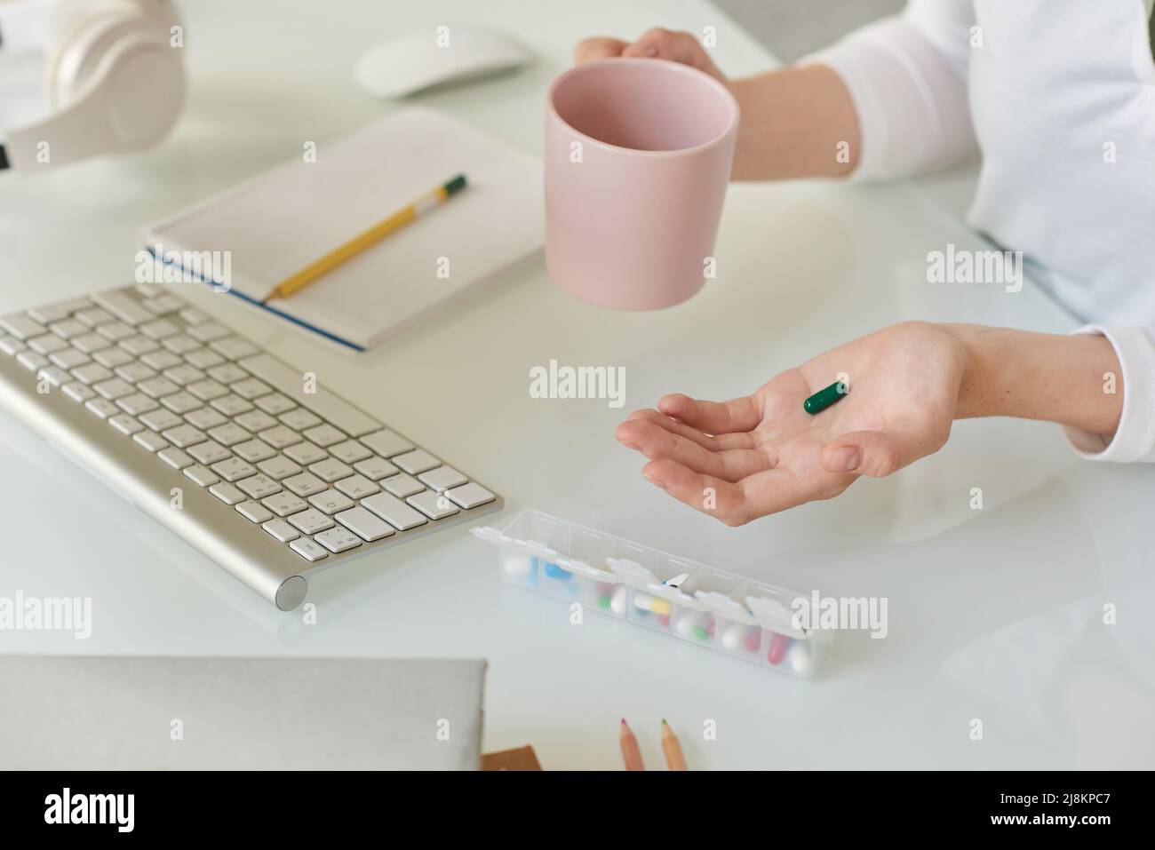 Close-up of unrecognizable manager sitting at table and drinking water while taking vitamin to increase brain function, biohacking concept Stock Photo