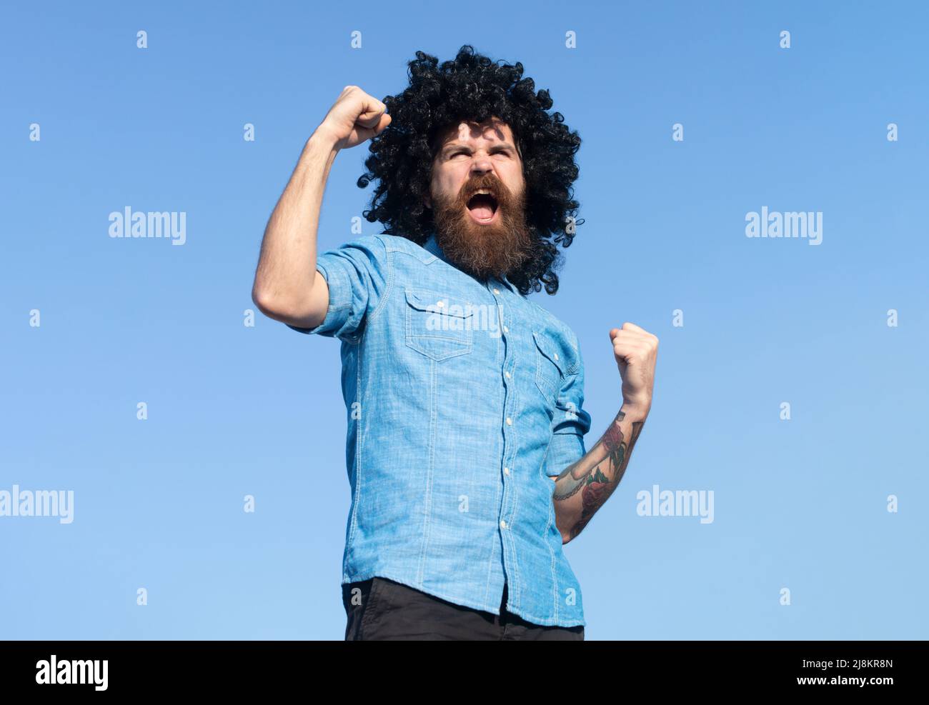 Funny nerdy guy. Crazy funny bearded man with wig on sky background