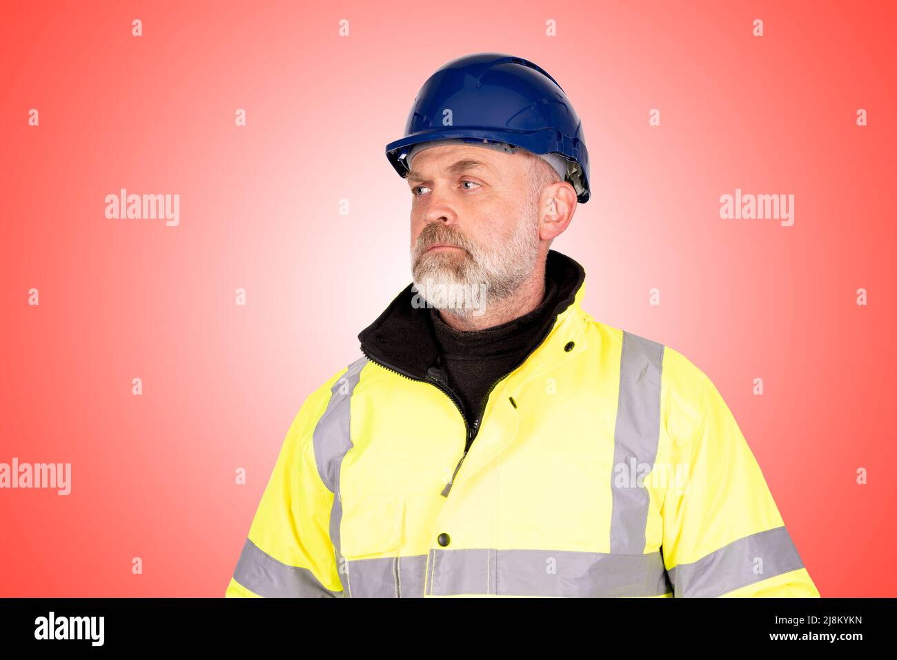 A construction worker in a blue hat and yellow hi-viz coat on a light red background Stock Photo