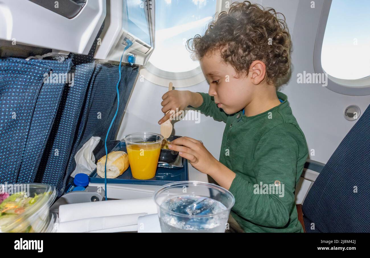 curly-haired boy with curly hair eating on airplane Stock Photo