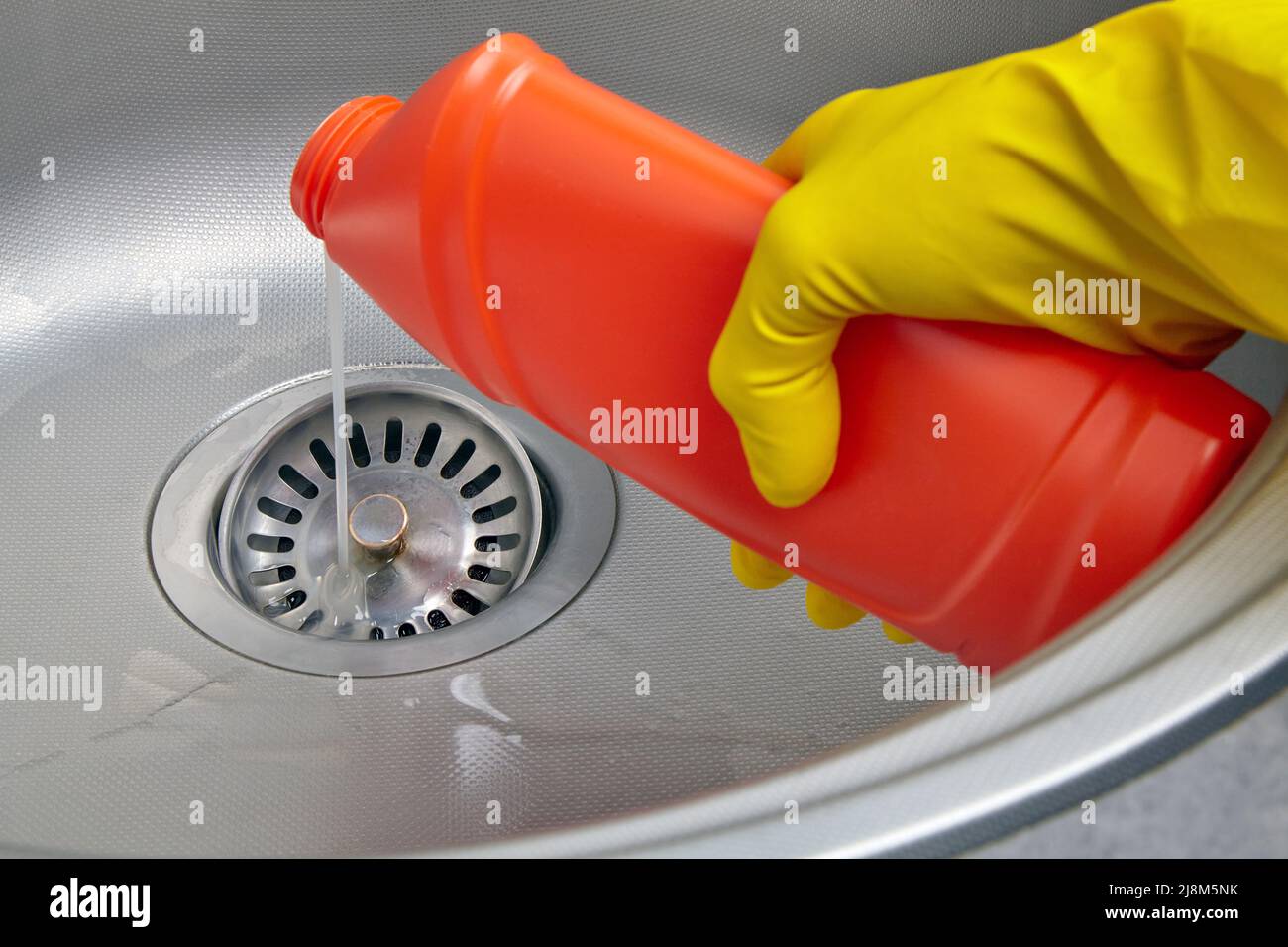 Hand in yellow rubber glove pour sewer pipe cleaner down the kitchen