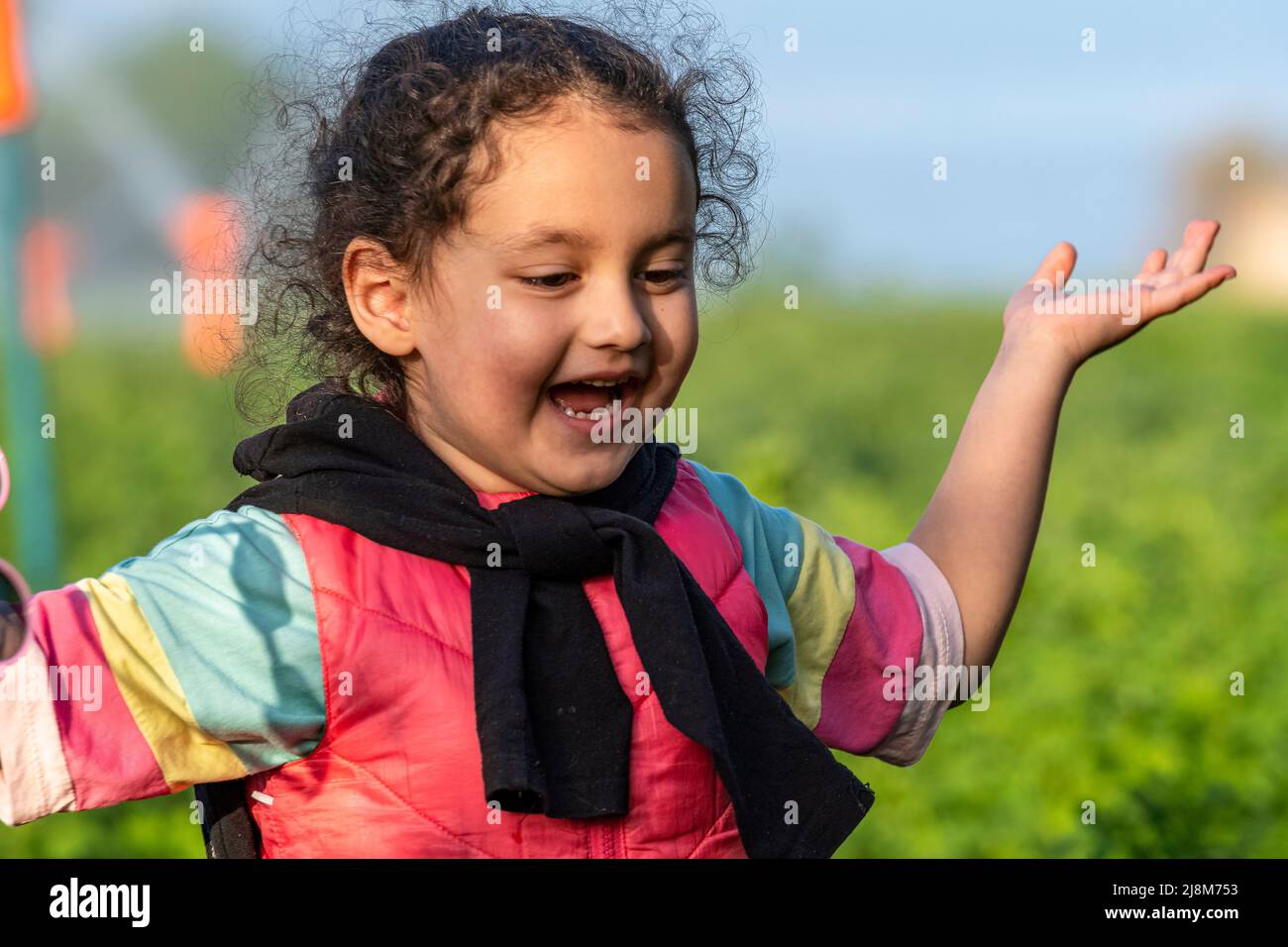 Selective focus shot of happy girl in pink outfit with black vest slung over her shoulder and open hands. Stock Photo