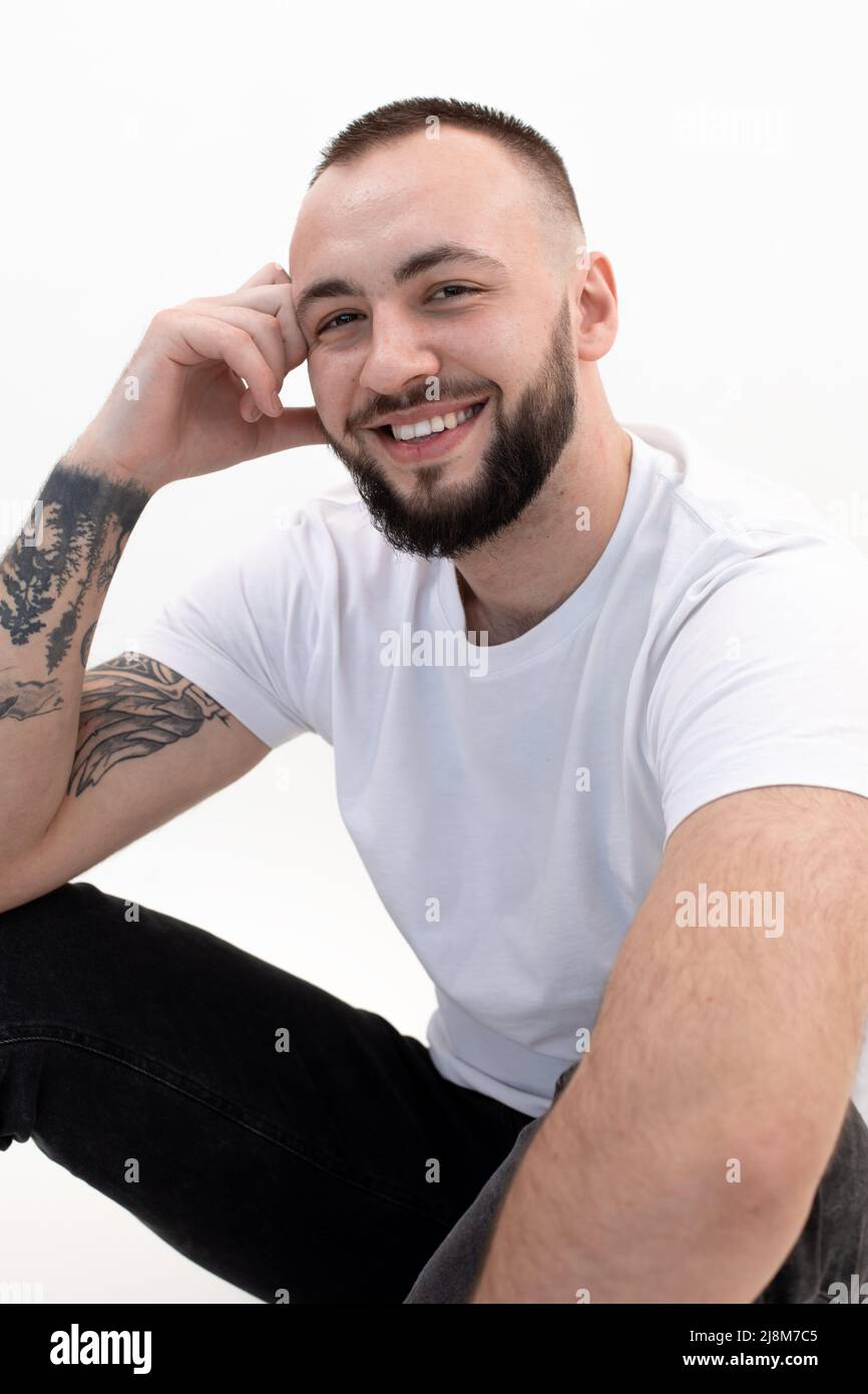 Vertical tattooed laughing handsome brunette man sitting in studio. Male hair loss problem. After transplanting. Closeup Stock Photo