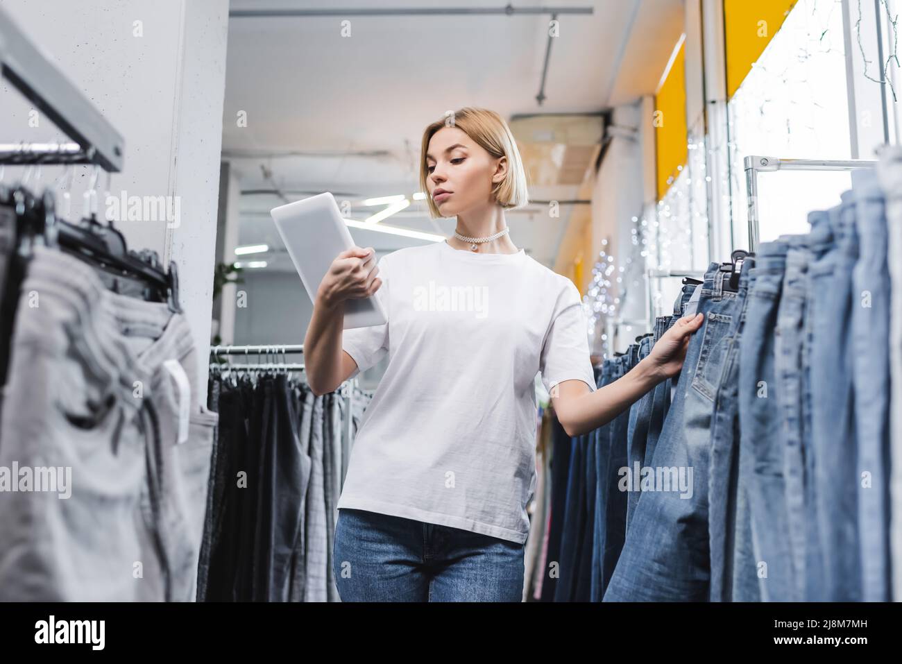 Low angle view of saleswoman looking at digital tablet near jeans in second hand Stock Photo