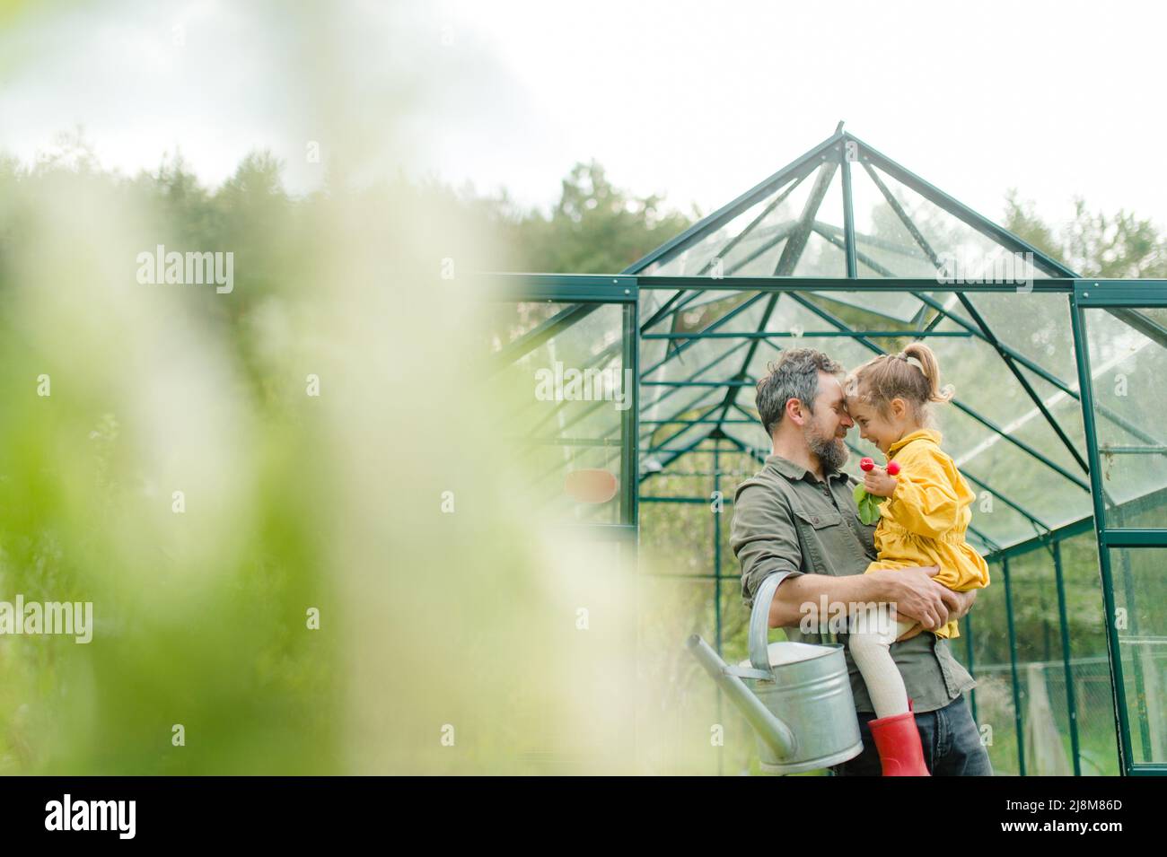 Father with his little daughter bonding in front of eco greenhouse, sustainable lifestyle. Stock Photo