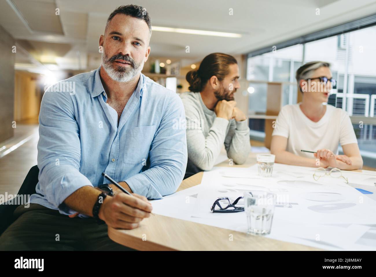Mature architect looking at the camera while sitting in a meeting with his team. Group of innovative businesspeople sharing creative ideas while worki Stock Photo