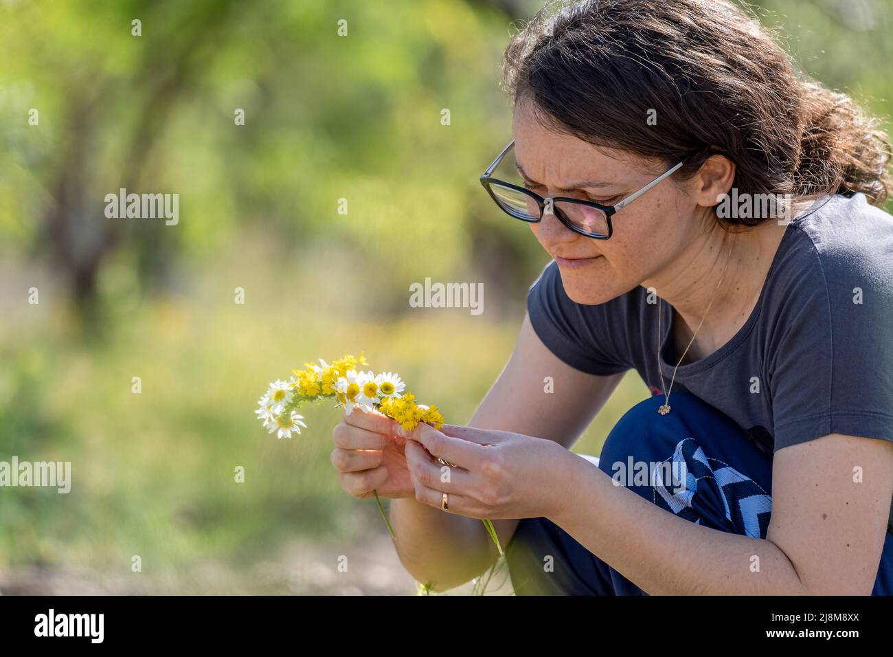 Selective focus shot of woman in glasses making crown from daisies. Stock Photo
