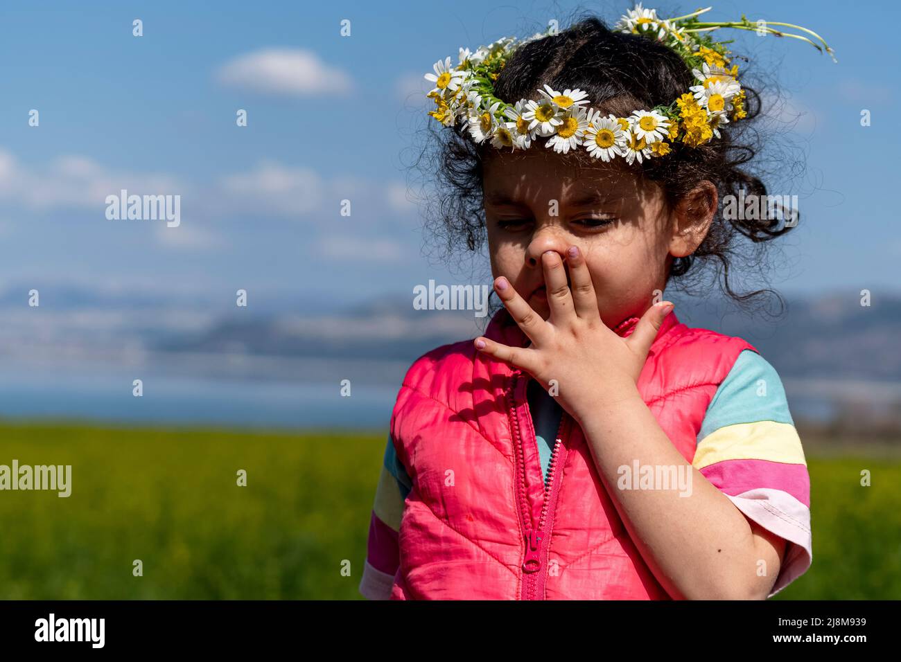 Selective focus shot from natural state of girl in colorful outfit wearing crown of daisies. Stock Photo