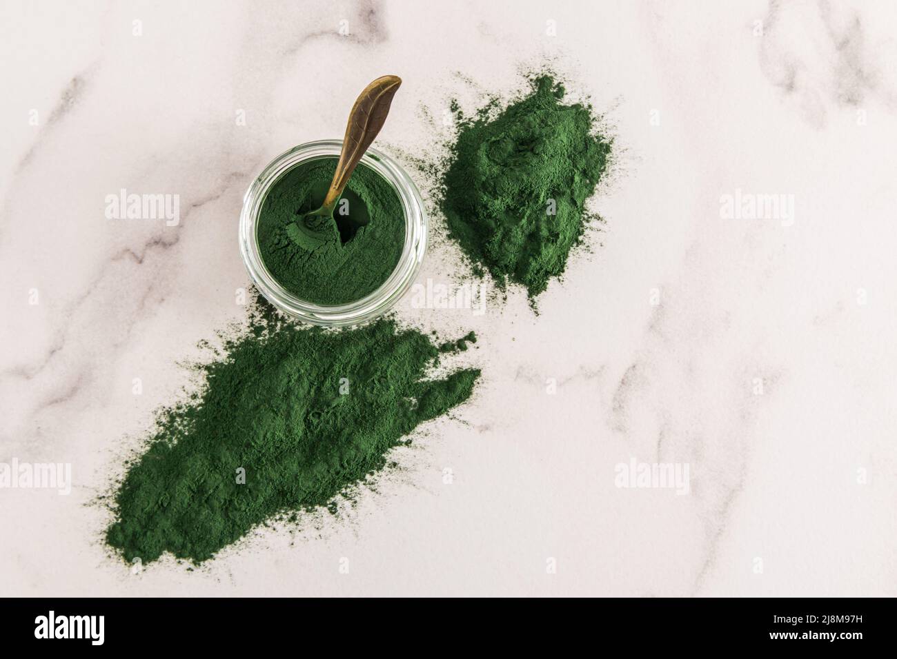 scattered spirulina powder on a marble white background and a glass jar with an organic food additive. cleansing the body of taxis Stock Photo