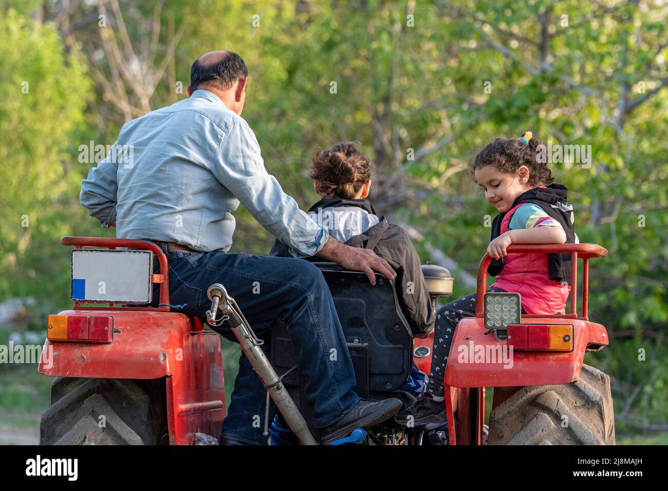 Closeup shot of grandfather, daughter and granddaughter on tractor ride with selective focus on background. Stock Photo