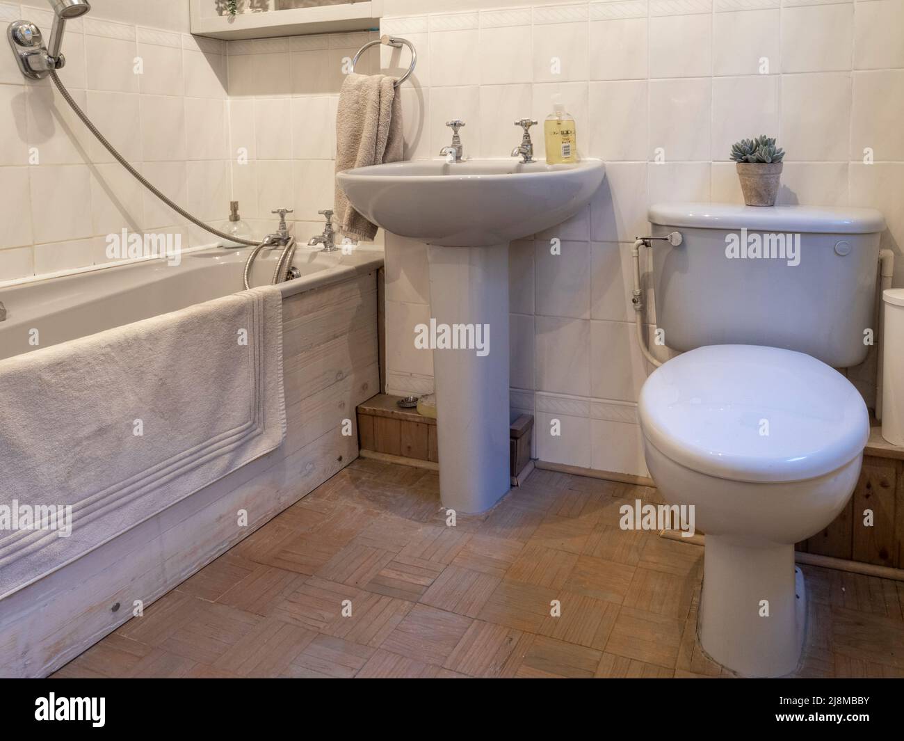 1980's style bathroom with brick pattern parquet floor, and grey bath, wash basin, and close couple toilet. Stock Photo