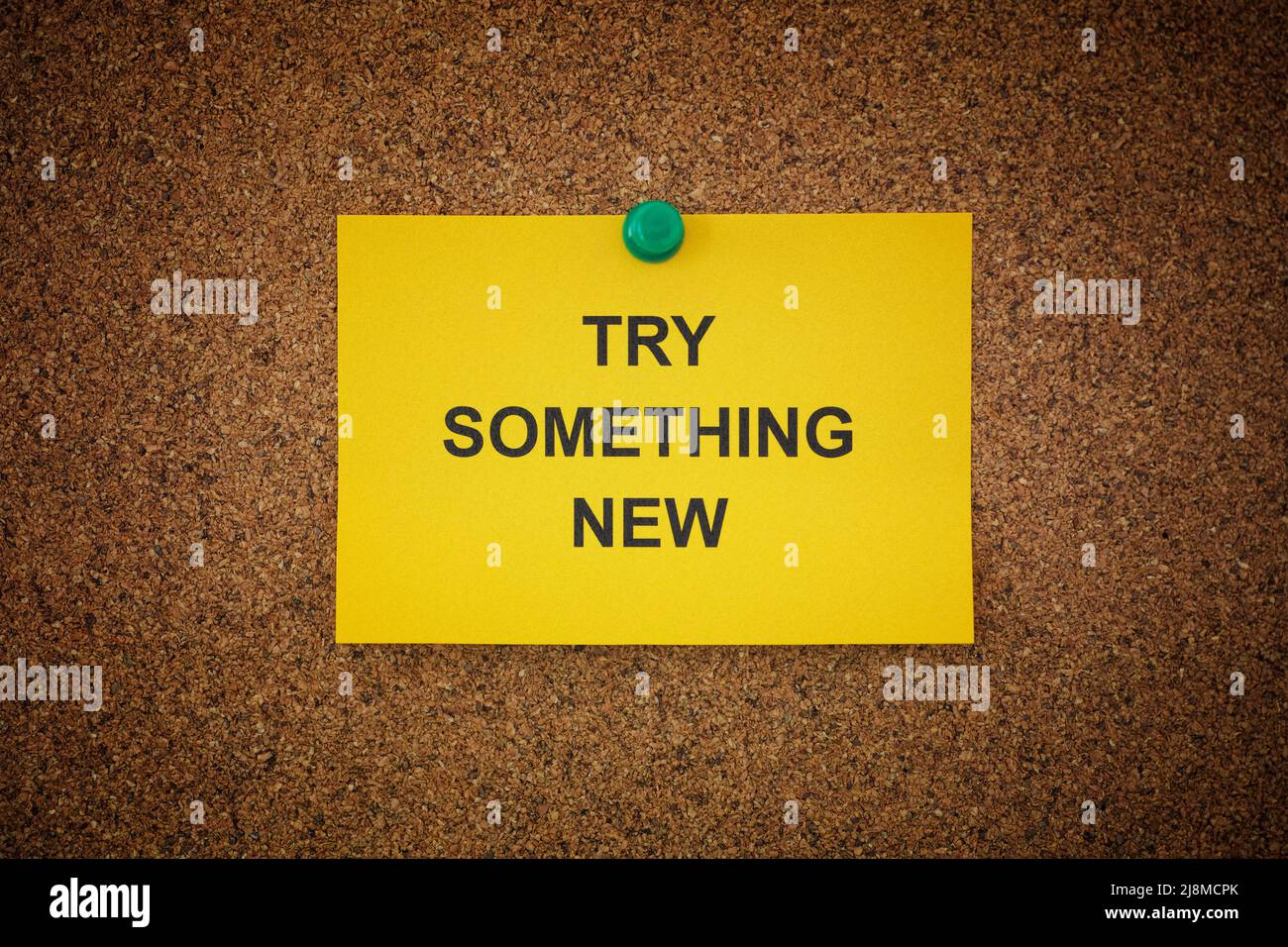 A sticky note with the words Try Something New on it pinned to a cork board. Close up. Stock Photo