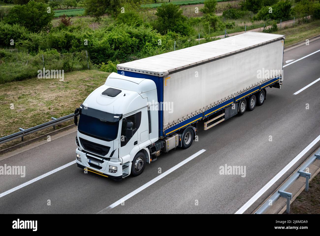 Big rig powerful professional industrial white semi truck for long haul delivery commercial cargo going with semi trailer on the summer road with fore Stock Photo