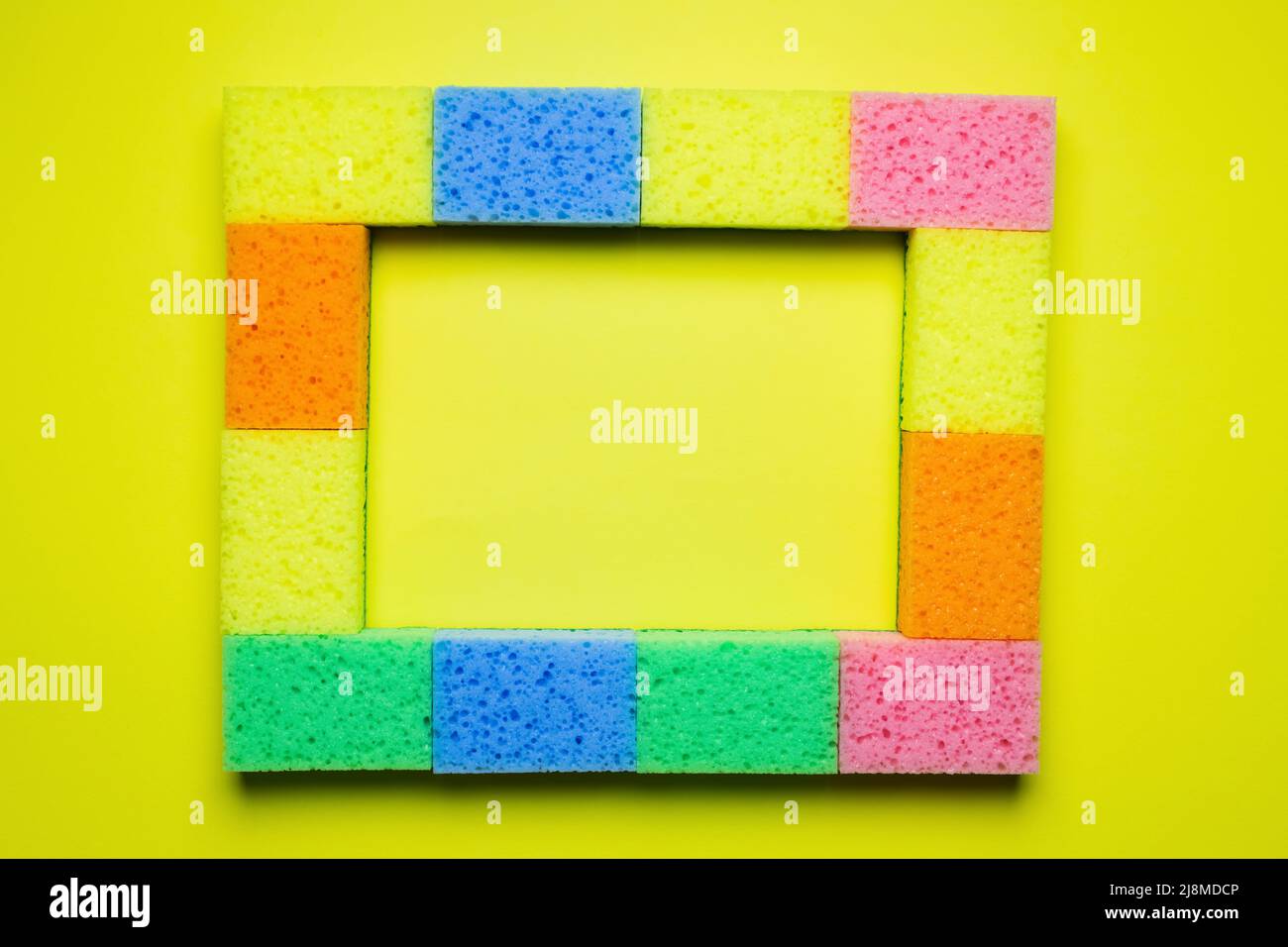 rectangular frame of multicolored sponges on yellow background, top view Stock Photo