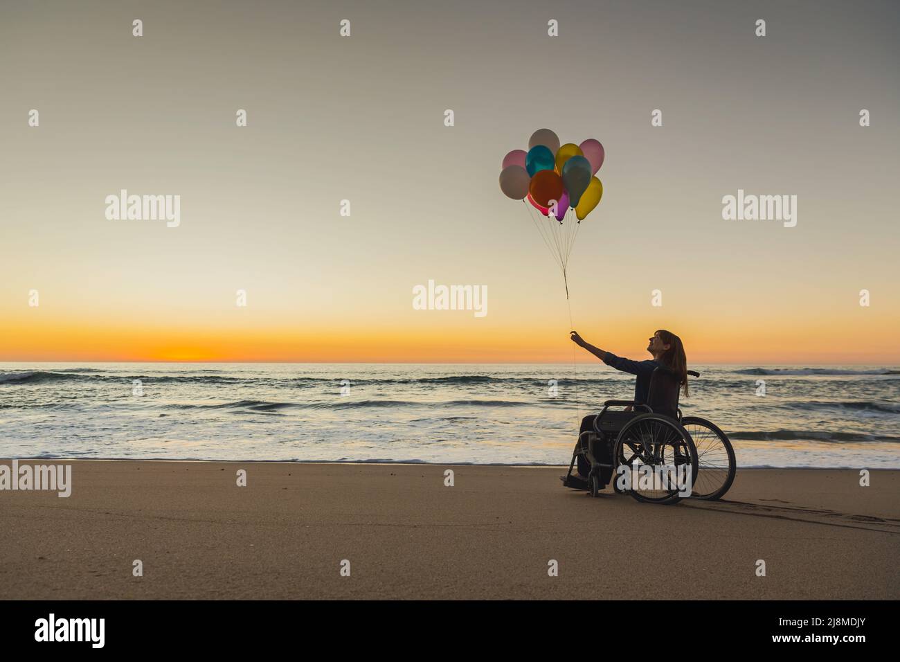 Handicapped woman on a wheelchair with colored balloons at the beach Stock Photo