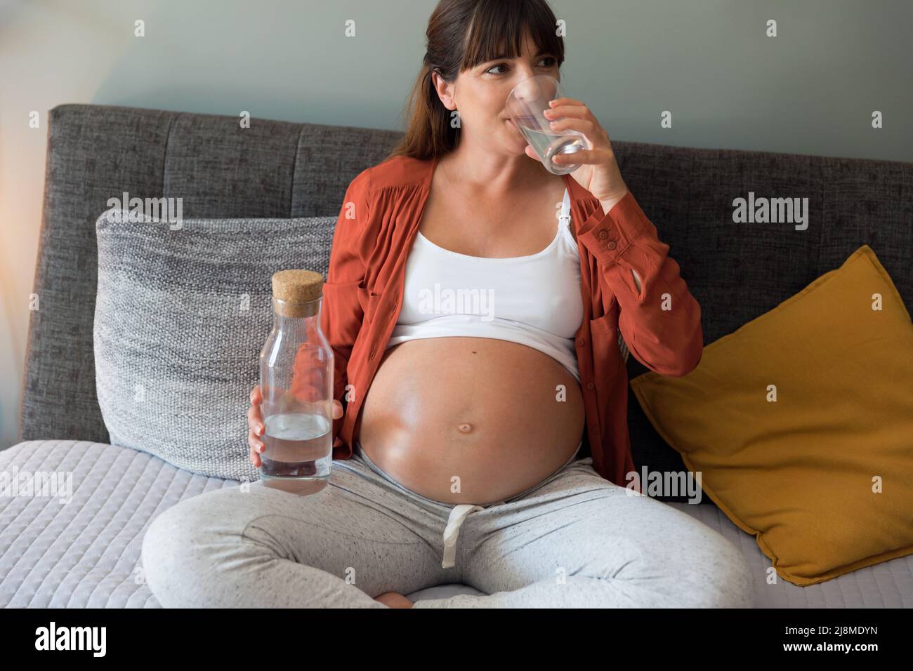 Pregnant woman holding glass of water relaxing in bed at home Stock Photo