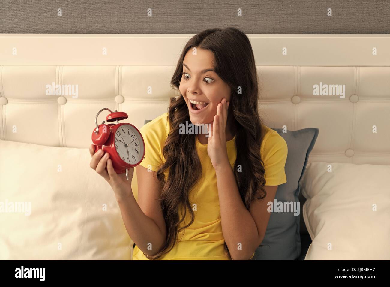 Shocked child look at alarm clock on waking in morning, shock Stock