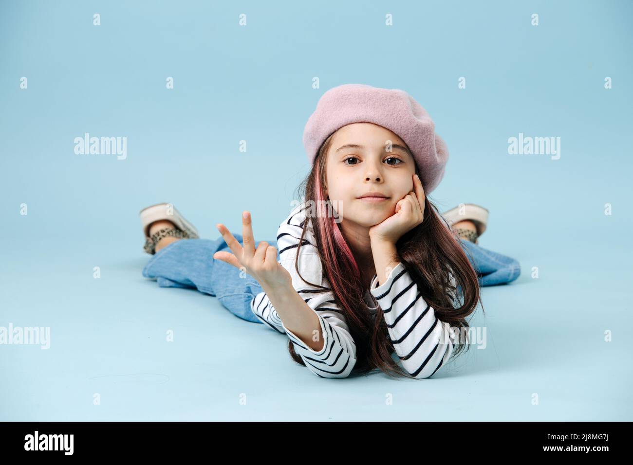Cool fashionable tween girl in french beret lying on the floor, showing ...