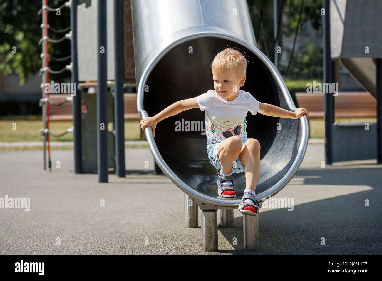 Joyful kid playing in tube slide on children's playground. Stock Photo