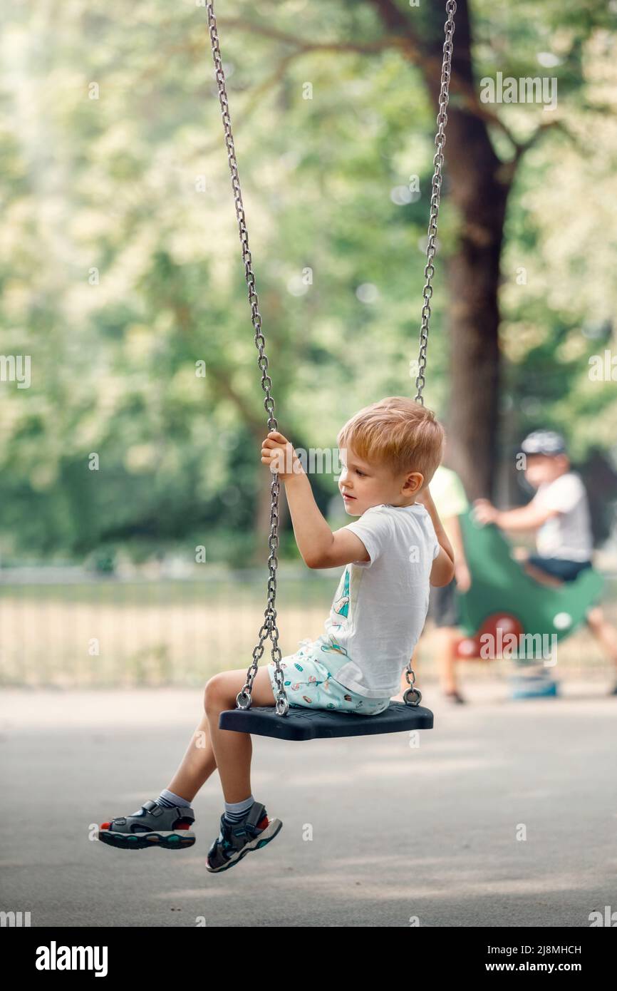 Happy little boy swinging on chain swing at playground. Stock Photo