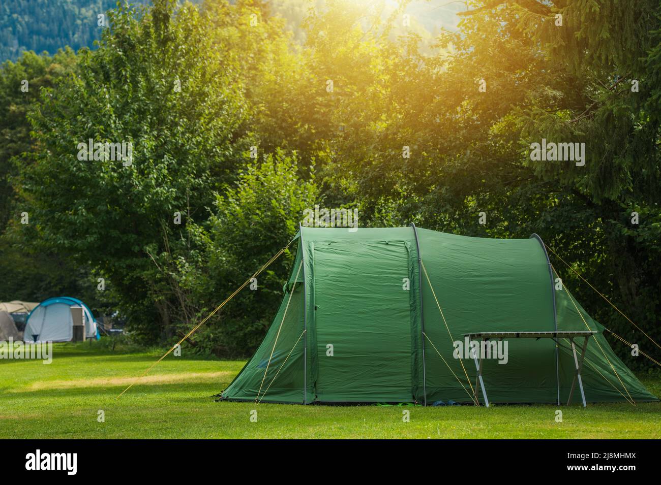 Summertime Vacation Tent Camping in the Nature. Large Green Tent and a Campsite Table. Stock Photo