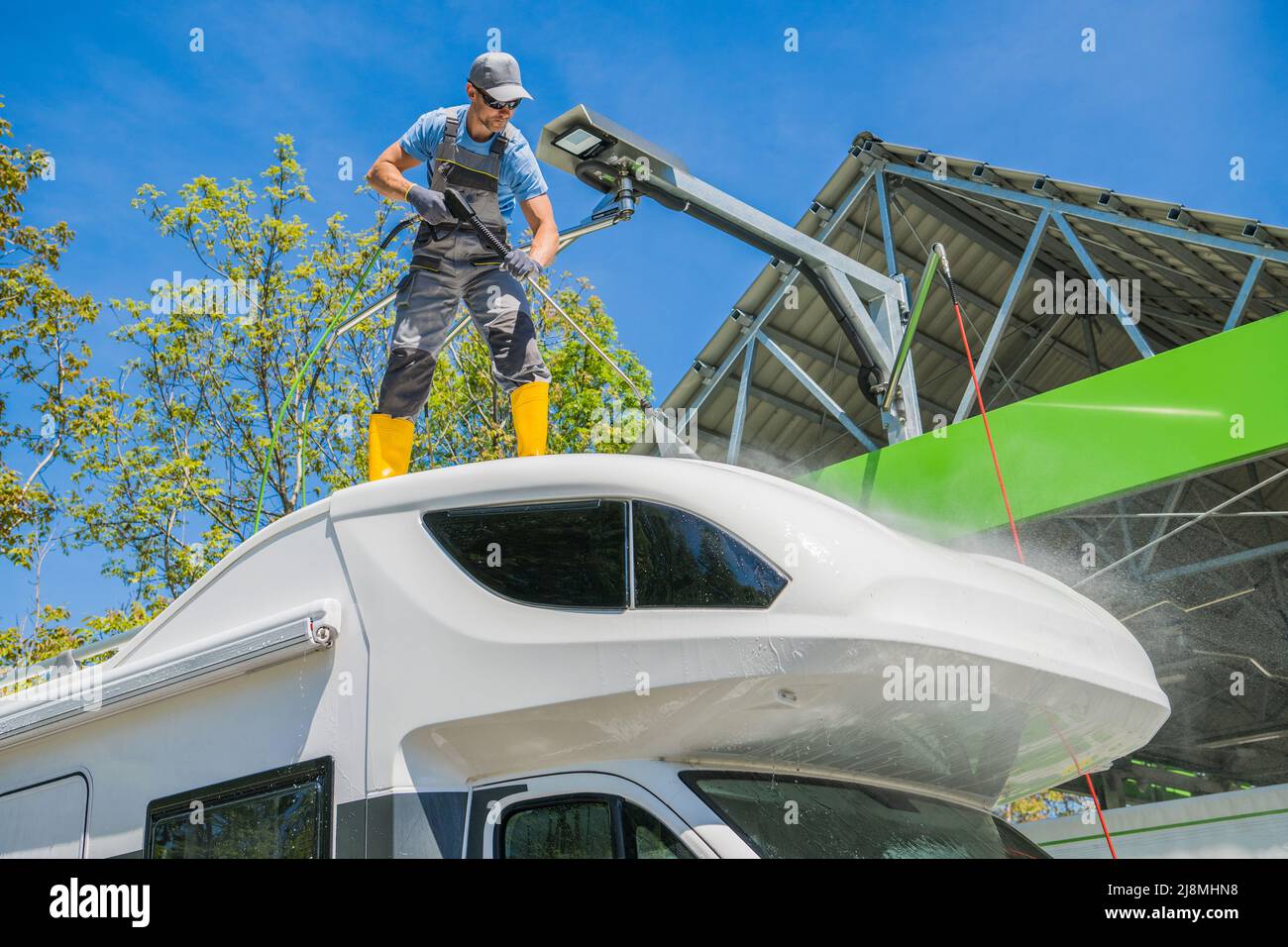 Caucasian RV Camper Rentals Worker Cleaning Motorhome Using Powerful Pressure Washer While Staying on the Vehicle Roof. Stock Photo