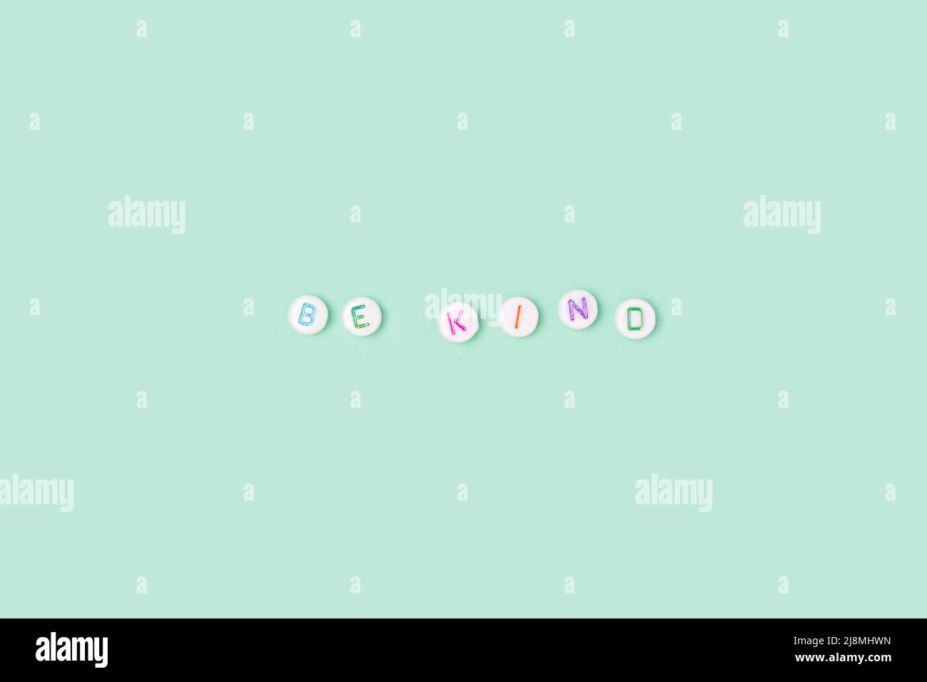 Be kind. Quote made of white round beads with colorful letters on a turquoise background. Stock Photo
