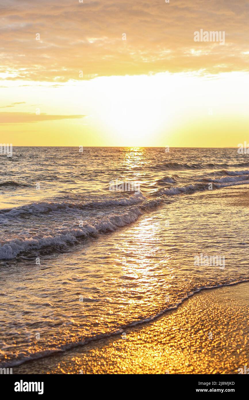 Sea waves on the seashore spill over the sandy sand in the evening at sunset Stock Photo