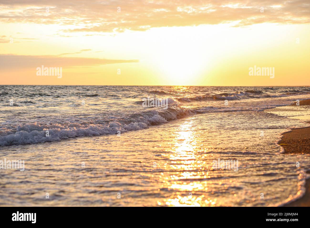 Sea waves on the seashore spill over the sandy sand in the evening at sunset Stock Photo