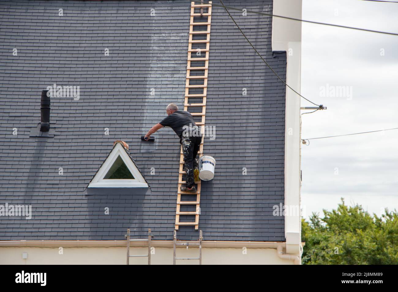 Worker spreading a product on a roof with a roller Stock Photo