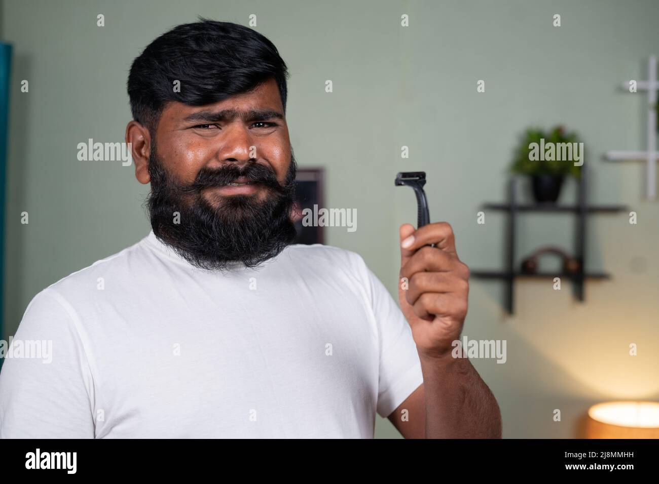 Young man saying no to shave the beard by holding razor and nodding head by looking at camera - concept of grooming and noshavember Stock Photo