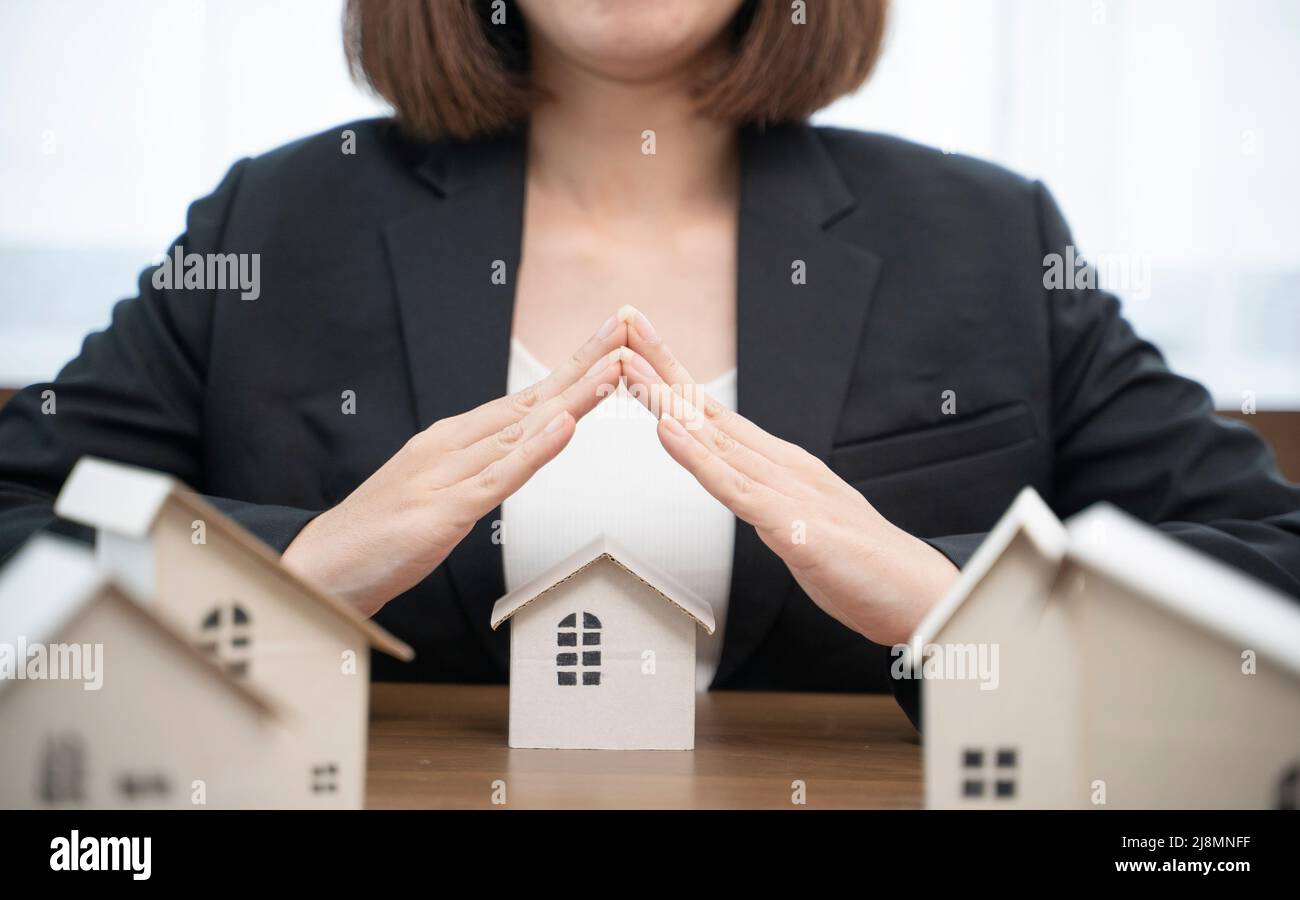 House covered by real estate insurance broker agent woman hands protecting gesture of man and symbol of house. Property insurance and security concept Stock Photo