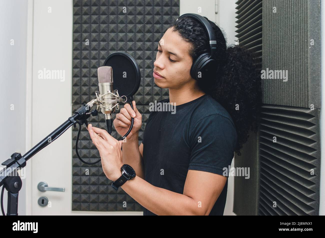 young singer man with headphones inside the professional studio in the recording booth, fixing the anti pop filter and the microphone to sing and reco Stock Photo