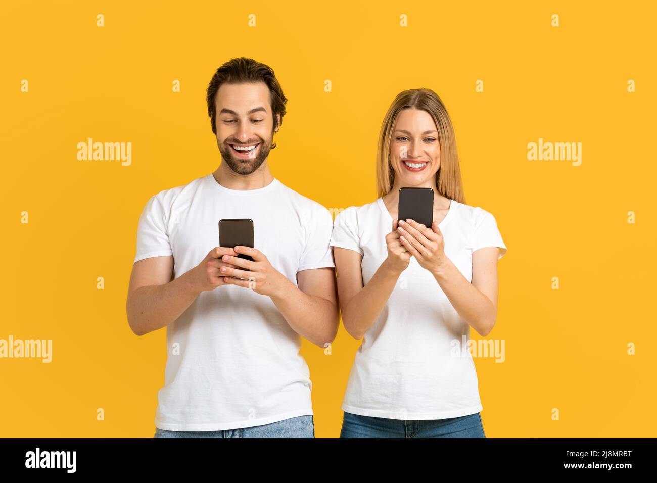 Smiling young european family in white t-shirts typing on phones, chatting in social networks Stock Photo