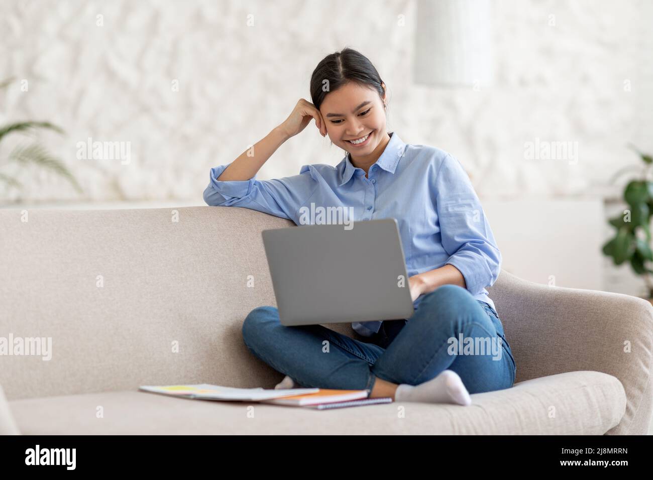 Happy young asian woman sitting on sofa with laptop Stock Photo