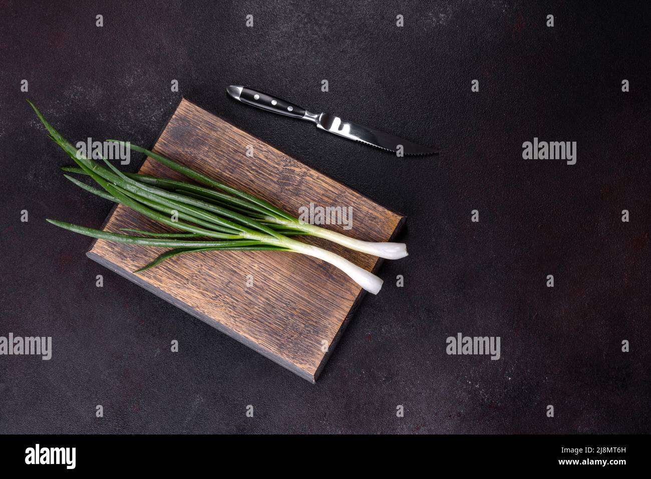 Cut Green onions chives on a cutting board. Dark concrete background ...
