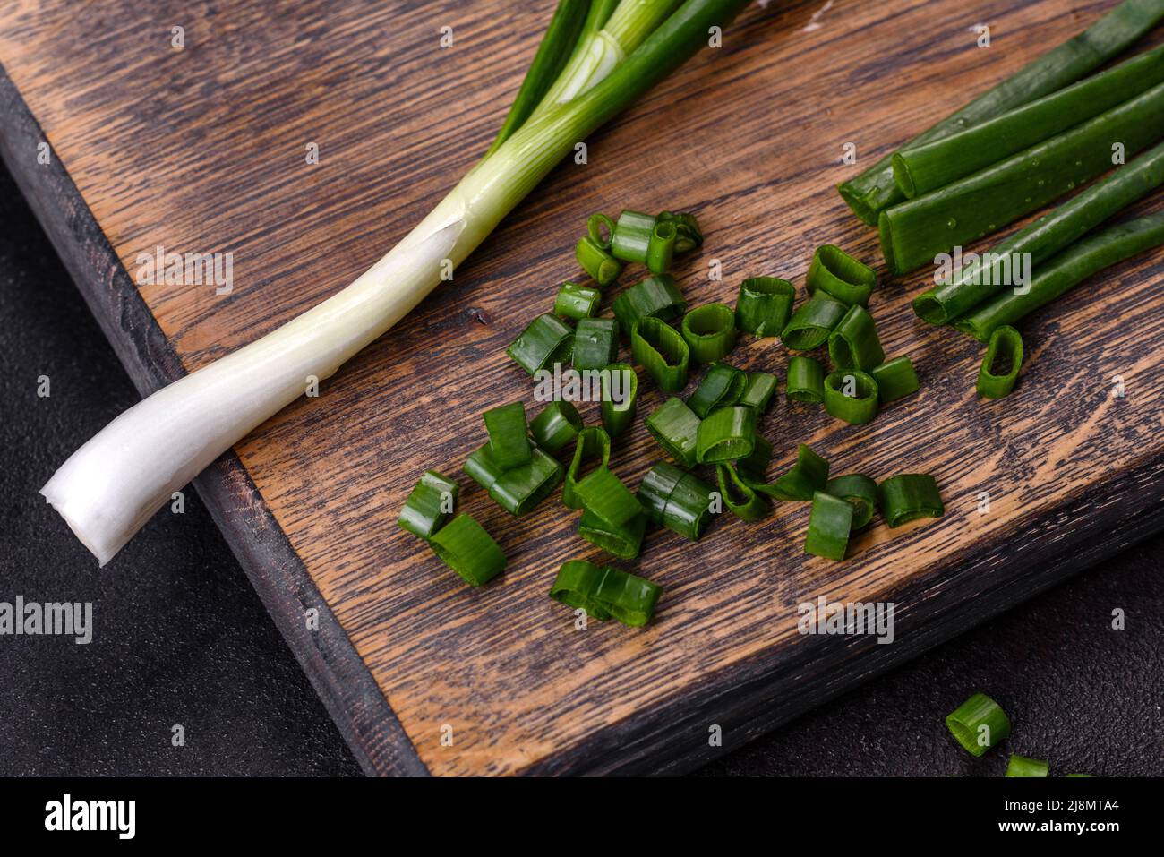 Cut Green onions chives on a cutting board. Dark concrete background ...