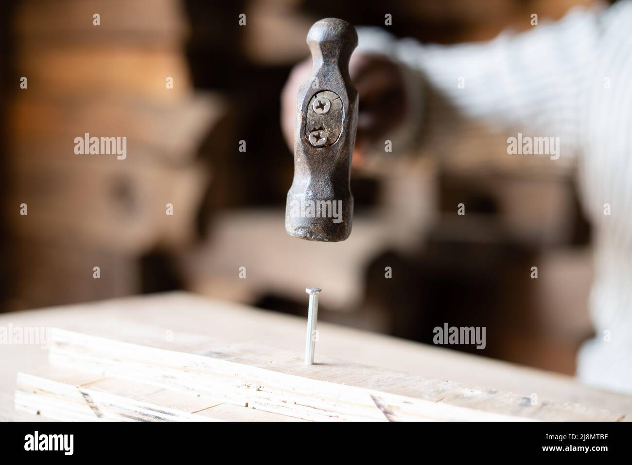 Close up shot of carpenter hands hitting nail to wood using hammer at shop - concept of workshop, woodworker and craftsman Stock Photo
