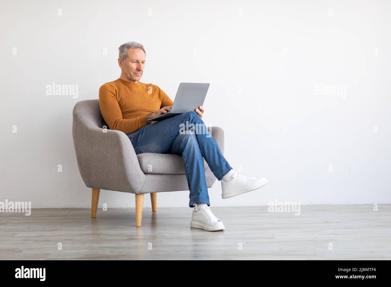 Confident mature man using laptop sitting on chair Stock Photo