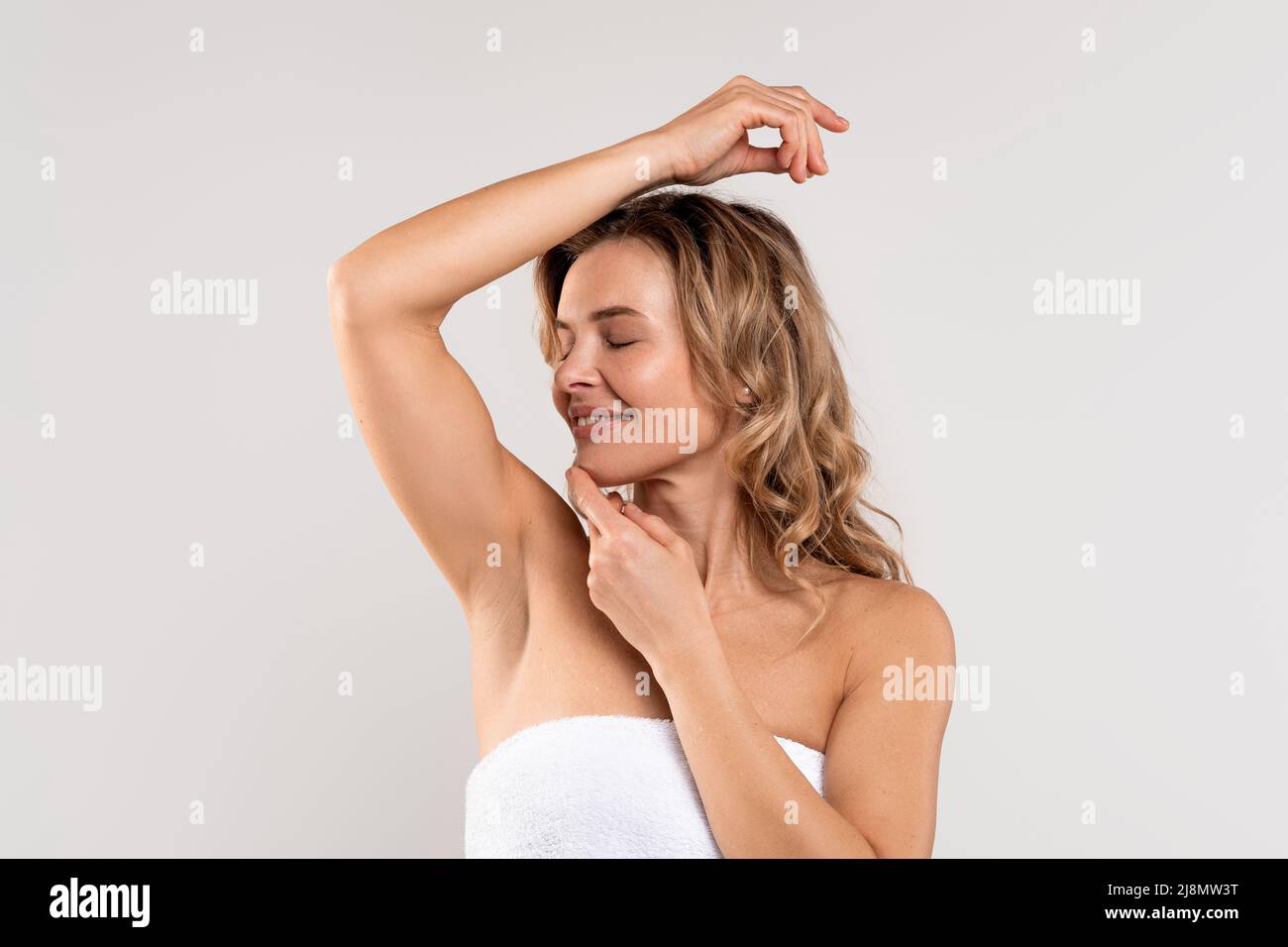 Beautiful caucasian woman smelling her fresh armpit while posing over grey background Stock Photo