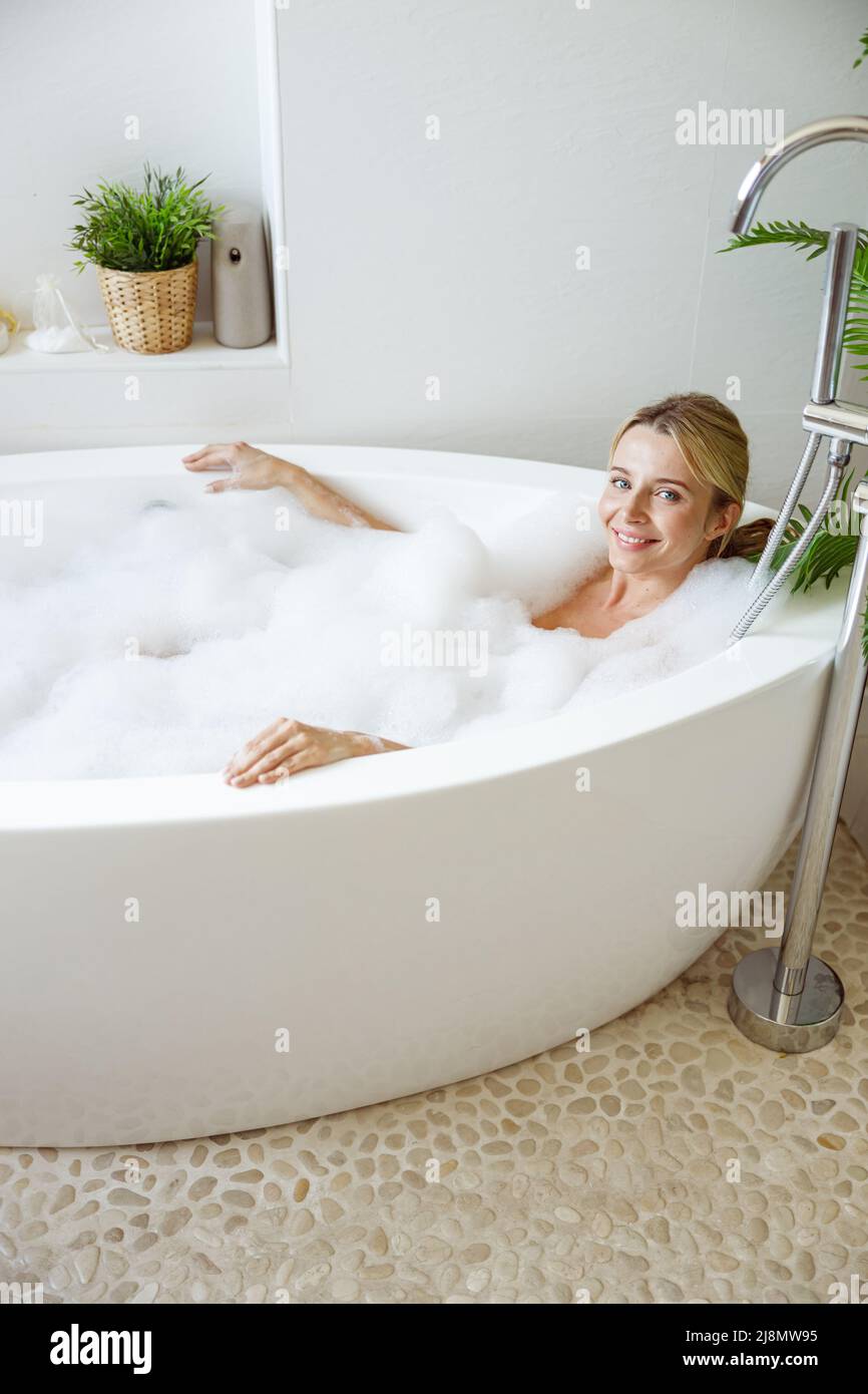 Portrait of happy beautiful young blonde female lying in hot bathtub in