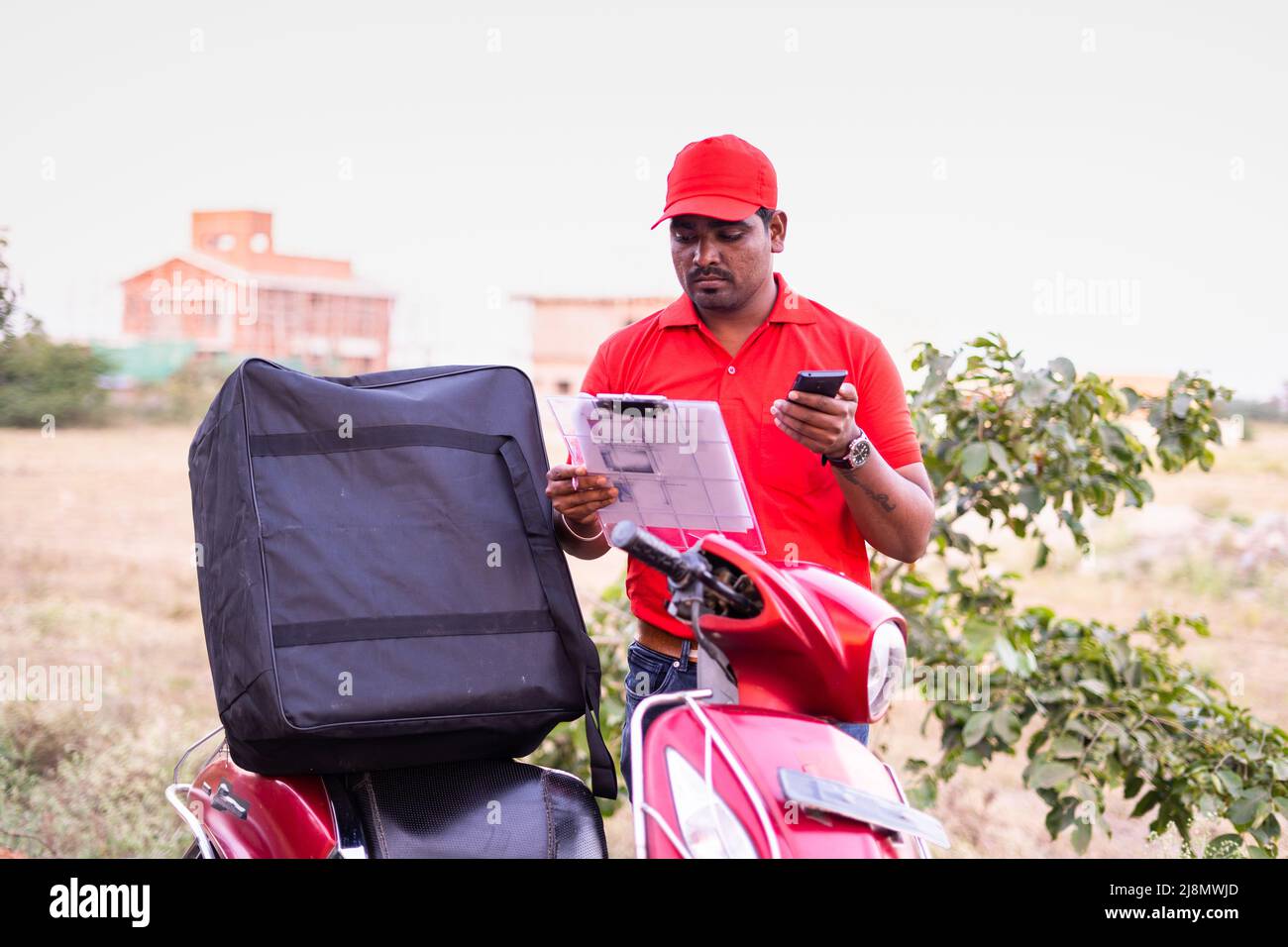 Indian delivery boy talking on mobile phone with customer while looking for address - concept of customer response, communication home delivery and Stock Photo