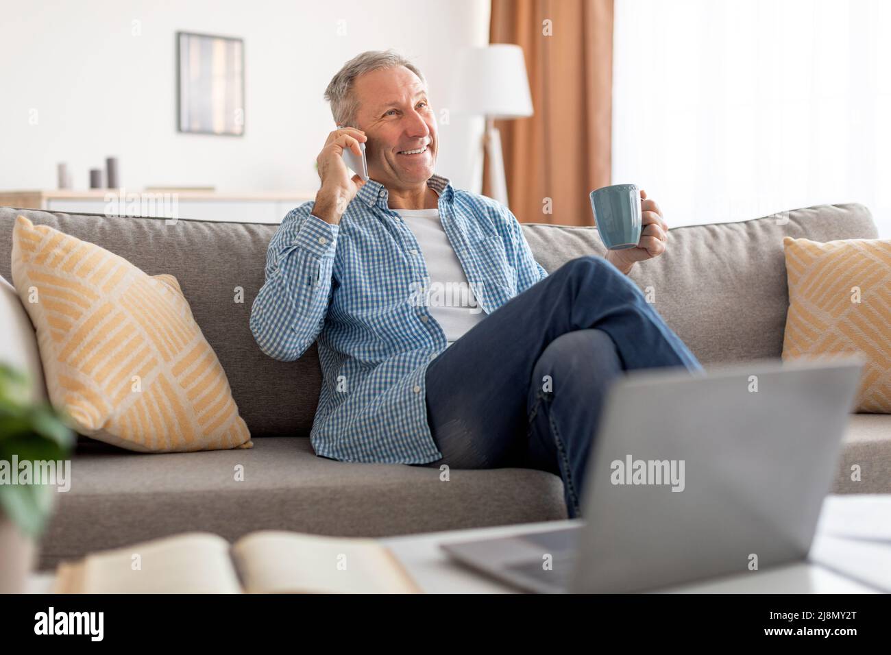 Cheerful mature man talking on cellphone sitting on sofa Stock Photo
